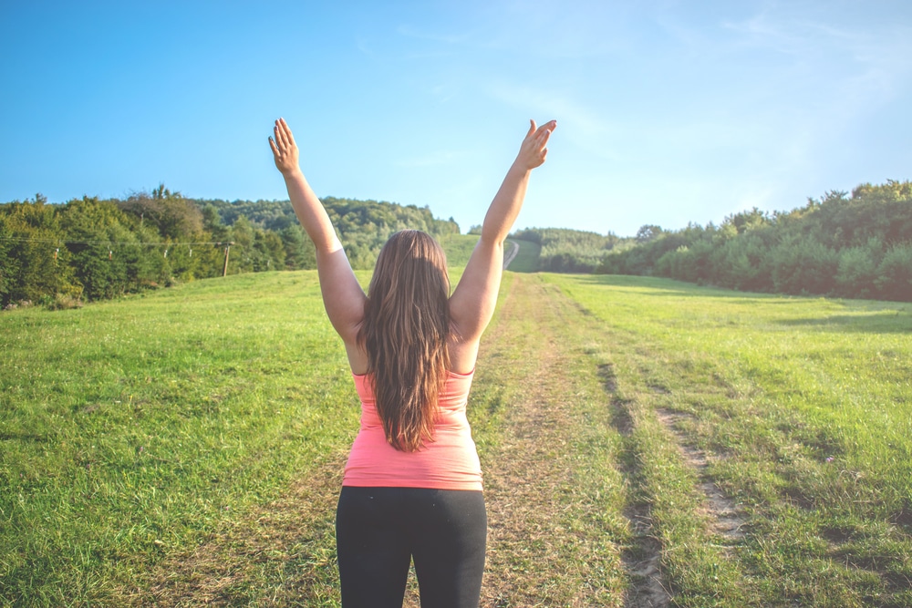 Woman lifts her arms in celebration outdoors because she's not experiencing pain.